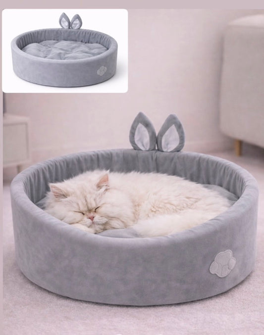 Gray pet bed with bunny ears and a white cat sleeping inside on a light gray floor.